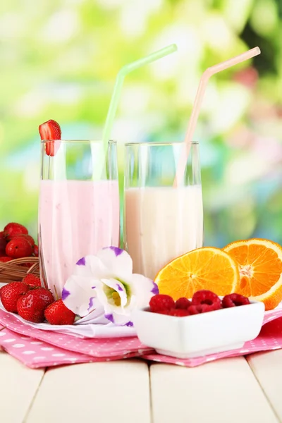 Delicious milk shakes with strawberries and orange on wooden table on natural background — Stock Photo, Image
