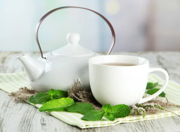 Teiera e tazza di tisana con fiori di menta freschi sul tavolo di legno — Foto Stock