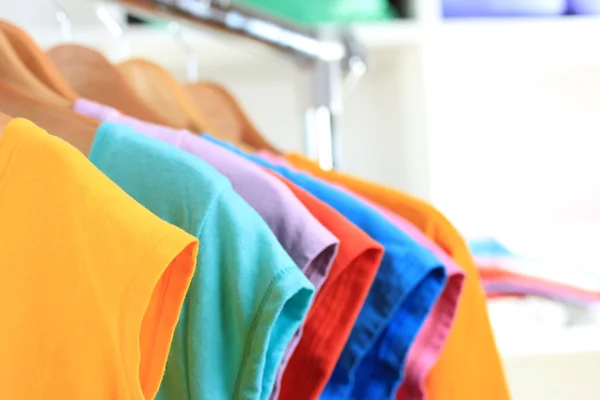 Variedade de camisetas casuais em cabides de madeira em prateleiras fundo — Fotografia de Stock