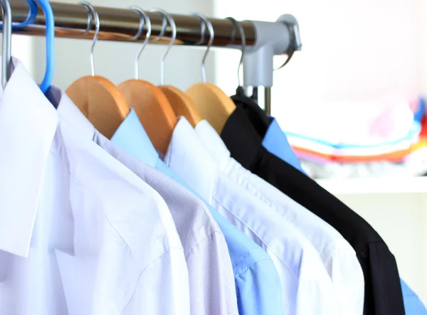 Variety of casual shirts on wooden hangers on shelves background — Stock Photo, Image