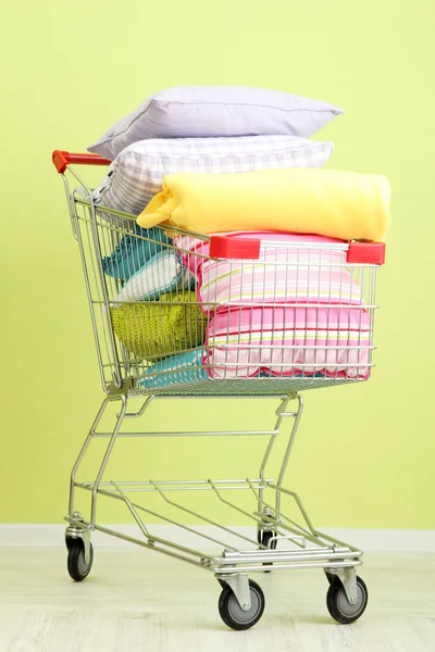 Shopping cart with pillows, on green wall background — Stockfoto