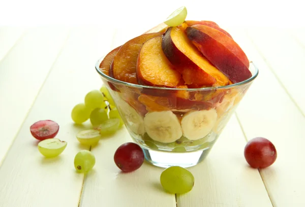 Salada de frutas saborosas em tigela de vidro, na mesa de madeira branca — Fotografia de Stock