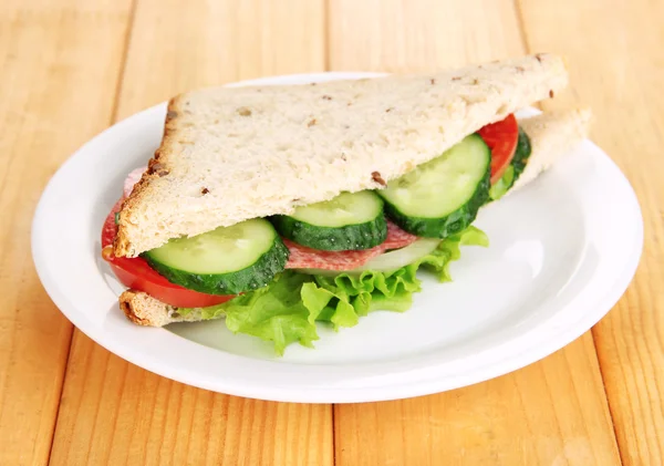 Sabroso sándwich con salchichas y verduras en plato blanco, sobre fondo de madera — Foto de Stock