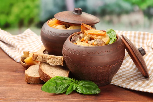 Roerbak zelfgemaakte rundvlees met groenten in potten op houten tafel, op lichte achtergrond — Stockfoto