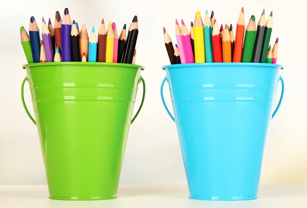 Кольорові відра з різнокольоровими олівцями на кольоровому фоні — стокове фото