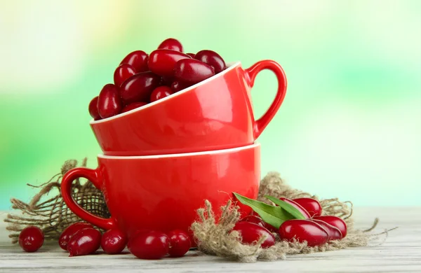 Fresh cornel berries in red cups on wooden table — Stock Photo, Image