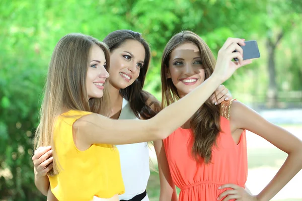 Три красивые девушки фотографируются в летнем парке — стоковое фото