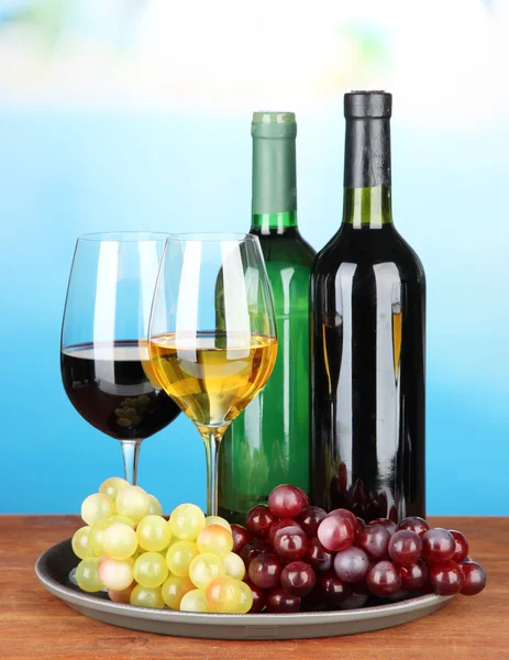 Wine bottles and glasses of wine on tray, on bright background — Stock Photo, Image