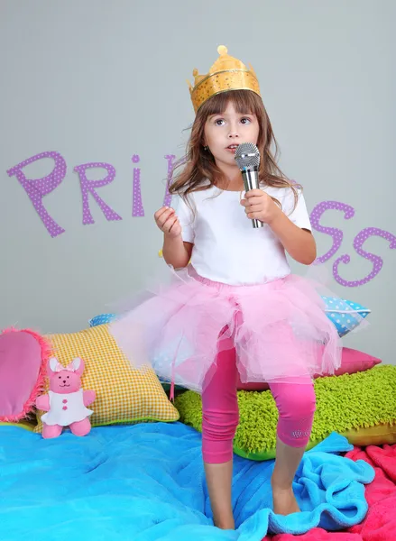 Маленька дівчинка танцює і співає на ліжку в кімнаті на сірому фоні стіни — стокове фото