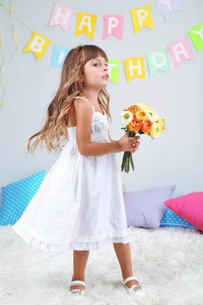 Little girl with flowers in room on grey wall background — Stock Photo, Image