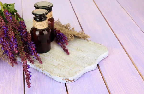 Geneeskundeflessen en salvia bloemen op paarse houten achtergrond — Stockfoto