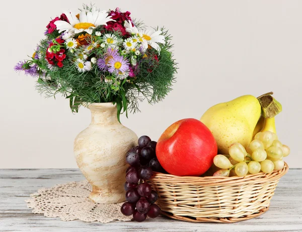 Kaunis kirkas kukkia maljakko hedelmiä pöydällä harmaalla pohjalla — kuvapankkivalokuva