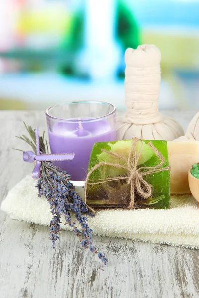 Bodegón con vela de lavanda, jabón, bolas de masaje, botellas, jabón y lavanda fresca, sobre una mesa de madera sobre fondo brillante — Foto de Stock