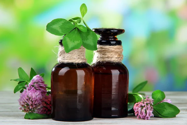 Medicine bottles with clover flowers on wooden table, outdoors — Stock Photo, Image