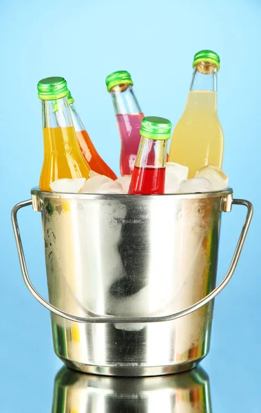 Garrafas com bebidas saborosas em balde com cubos de gelo, em fundo brilhante — Fotografia de Stock
