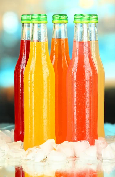 Bottles with tasty drinks with ice cubes, on bright background — Stock Photo, Image