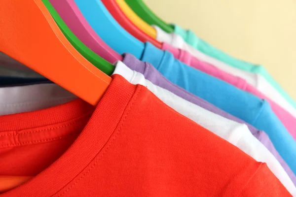 Different shirts on colorful hangers on beige background — Stock Photo, Image