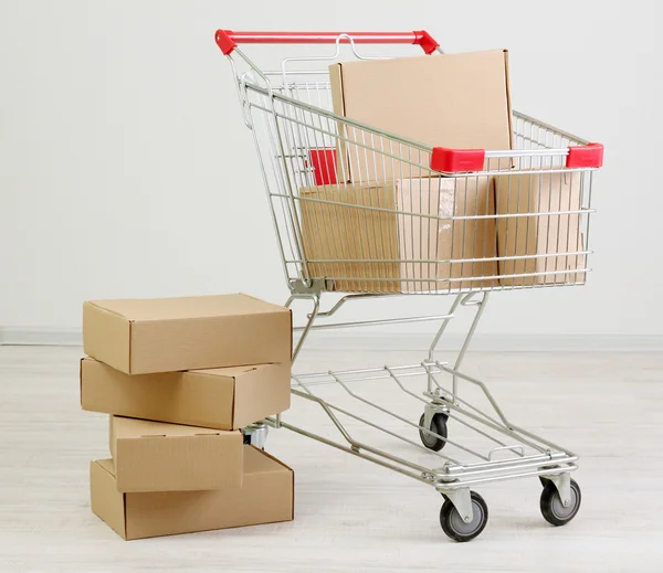 Shopping cart with carton, on gray background — Stock Photo, Image