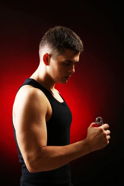 Pohledný mladý svalnatý sportovec s expandér, na tmavém pozadí — Stock fotografie
