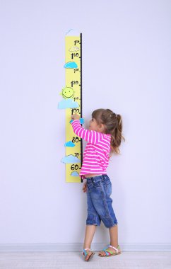 Little girl measuring height against wall in room clipart