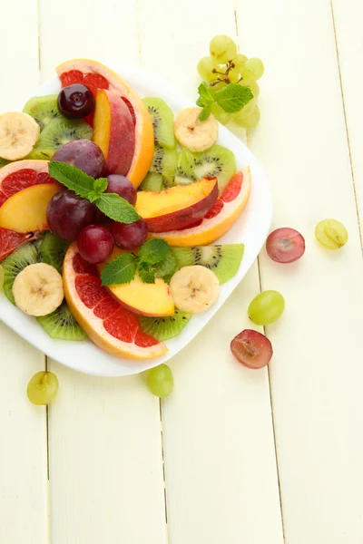 Surtido de frutas en rodajas en plato, sobre mesa de madera blanca — Foto de Stock