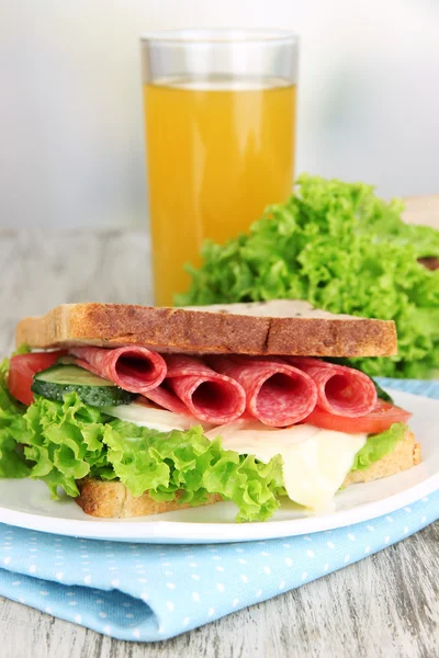 Composition with fruit juice and tasty sandwich with salami sausage and vegetables on color napkin, on wooden table, on bright background — Stock Photo, Image