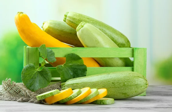 Sliced and whole raw zucchini in wooden crate, outdoors — Stock Photo, Image