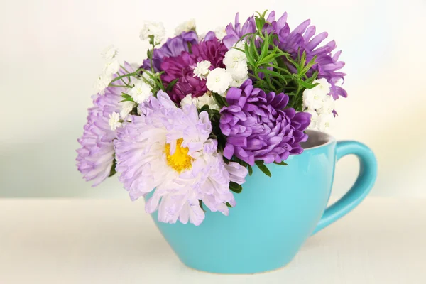 Belo buquê de flores brilhantes na caneca de cor, na mesa de madeira, no fundo claro — Fotografia de Stock
