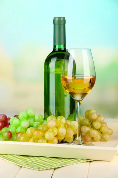 Wine bottle and glass of wine on tray, on bright background — Stock Photo, Image