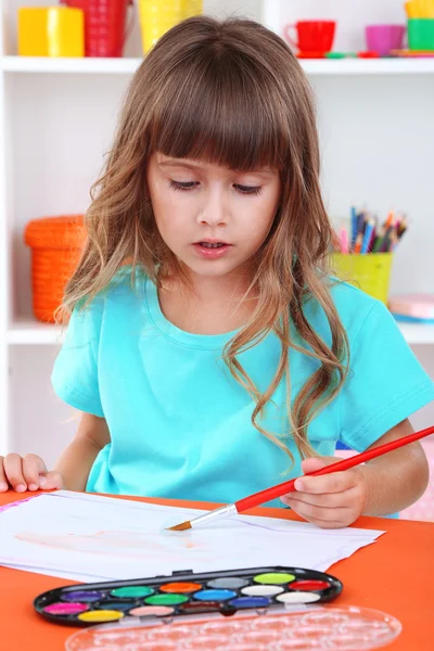 Little girl draws sitting at table in room on shelves background — Stock Photo, Image