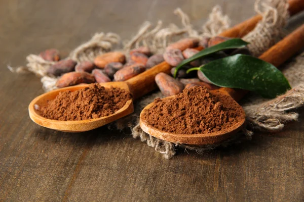 Cacao en polvo y frijoles en cucharas sobre fondo de madera — Foto de Stock