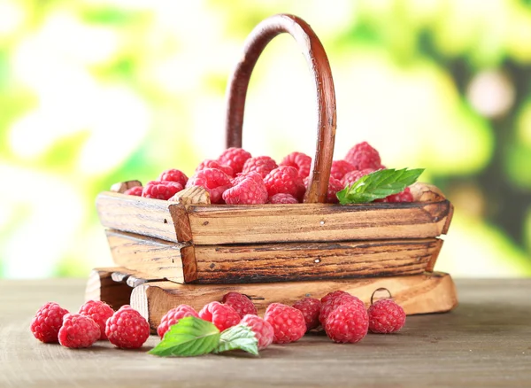 Ripe sweet raspberries in basket on wooden table, on green background — Stock Photo, Image