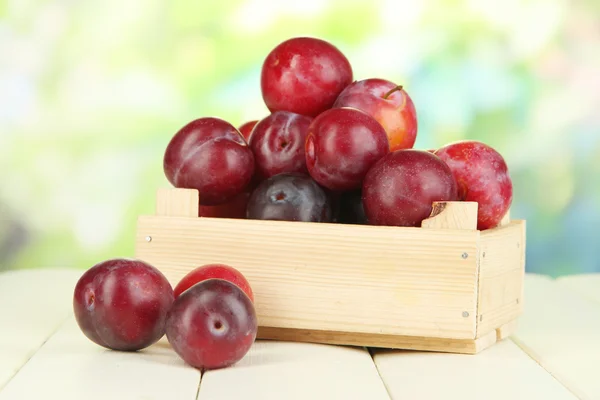 Ripe plums in wooden box on wooden table on natural background — Stock Photo, Image