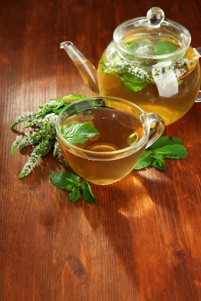 Чашка и чайник травяного чая со свежими мятными цветами на деревянном столе — стоковое фото