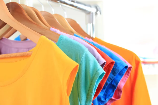 Variety of casual t-shirts on wooden hangers on shelves background — Stock Photo, Image