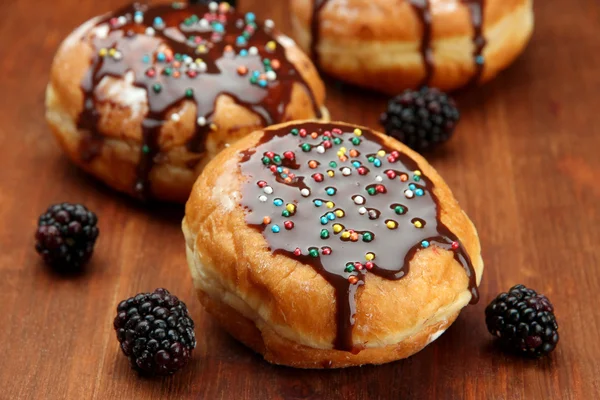 Smakelijke donuts met chocolade en bessen op houten tafel — Stockfoto