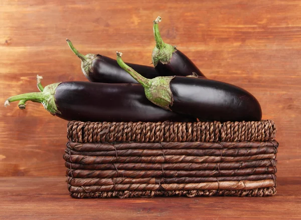 Fresh eggplants in wicker basket on table on wooden background — Stock Photo, Image