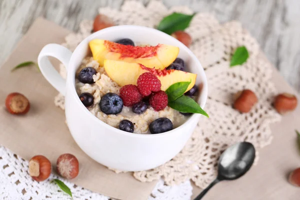 Harina de avena en taza con bayas en servilletas sobre mesa de madera —  Fotos de Stock