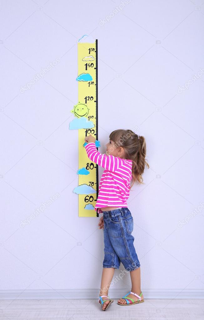 Little girl measuring height against wall in room