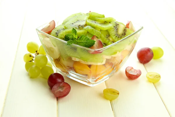 Smakelijke fruitsalade in glazen kom, op witte houten tafel — Stockfoto