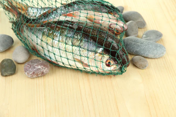 Fishes in fishing net on wooden background — Stock Photo, Image