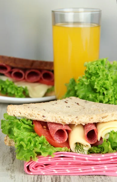 Compositie bij vruchtensap en lekkere sandwich met worst salami en groenten op kleur servet, op houten tafel, op lichte achtergrond — Stockfoto