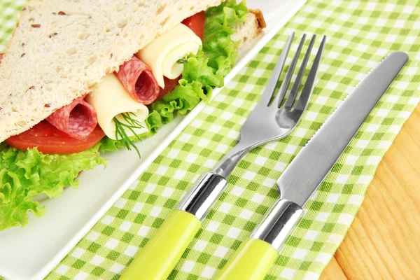 Tasty sandwich with salami sausage and vegetables on white plate, on wooden background — Stock Photo, Image