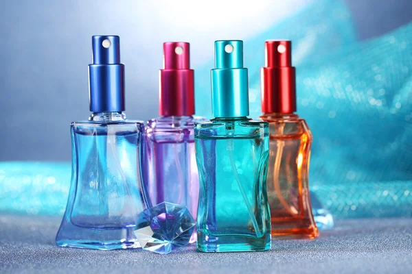 Perfume de mujer en hermosas botellas sobre fondo azul — Foto de Stock