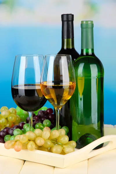 Wine bottles and glasses of wine on tray, on bright background — Stock Photo, Image