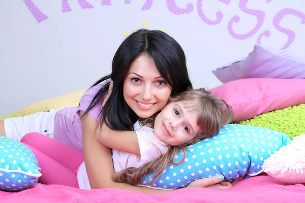 Menina com a mãe deitada na cama no quarto no fundo da parede cinza — Fotografia de Stock