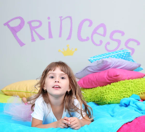 Little girl lying on bed in room on grey wall background — Stock Photo, Image