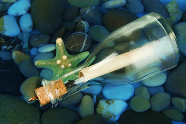 Bottle with letter on sea bottom with shells and stones — Stock Photo, Image