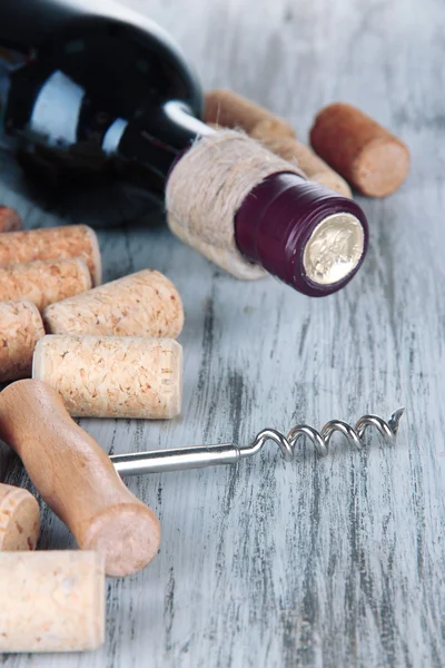 Corkscrew with wine corks and bottle of wine on wooden table close-up — Stock Photo, Image