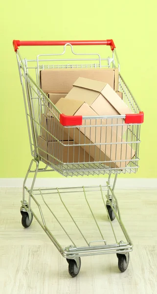 Shopping cart with carton, on green wall background — Stock Photo, Image